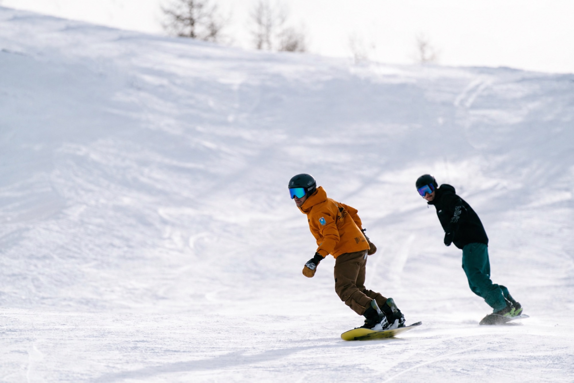 Maestro Preskige col casco, in giacca arancione, che scende in snowboard accanto all'allievo a Sestriere
